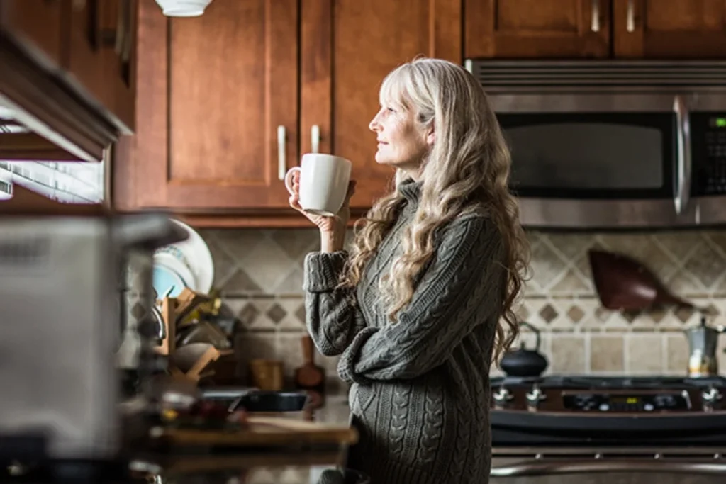 woman drinking a cup of coffee in the kitchen while she looks out the window