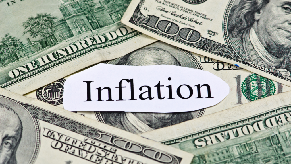 the word "inflation" typed on a piece of paper laying over dollar bills