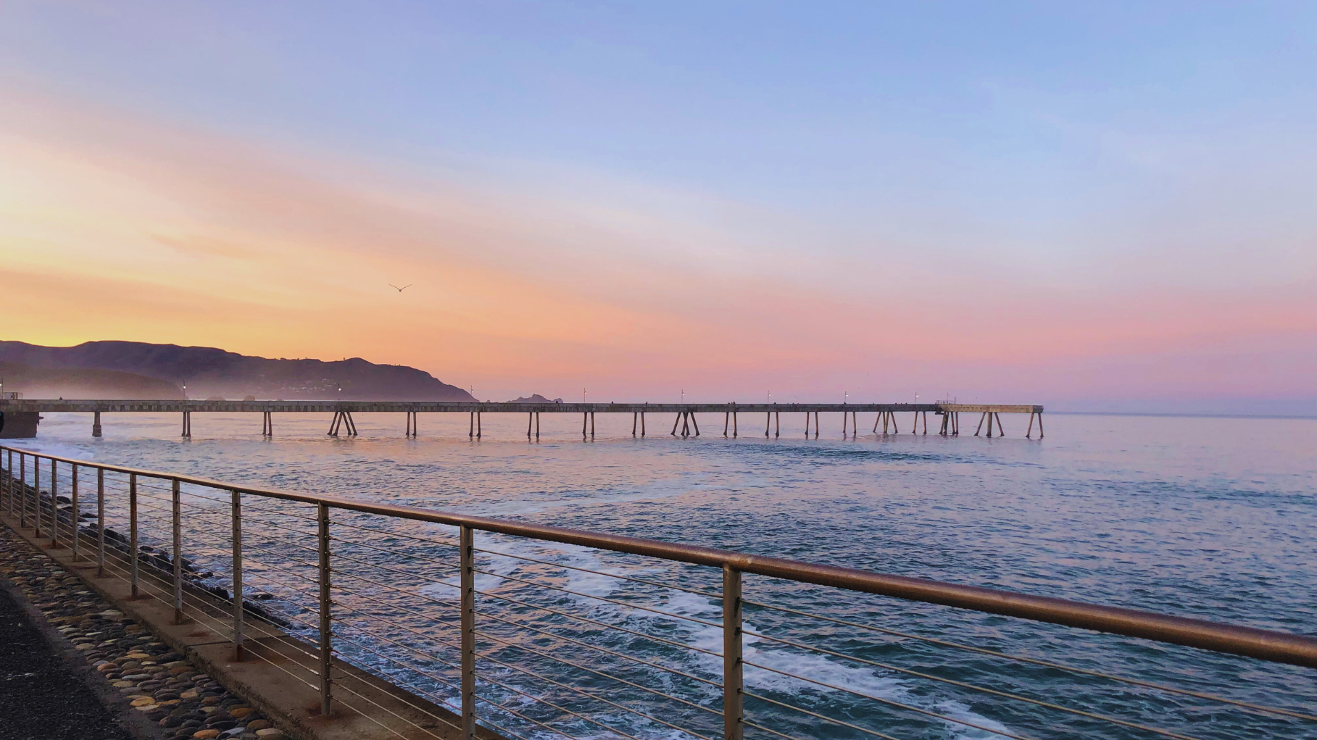 Pacifica Pier at sunset with ocean waves and glowing sky. coastal California landmark.